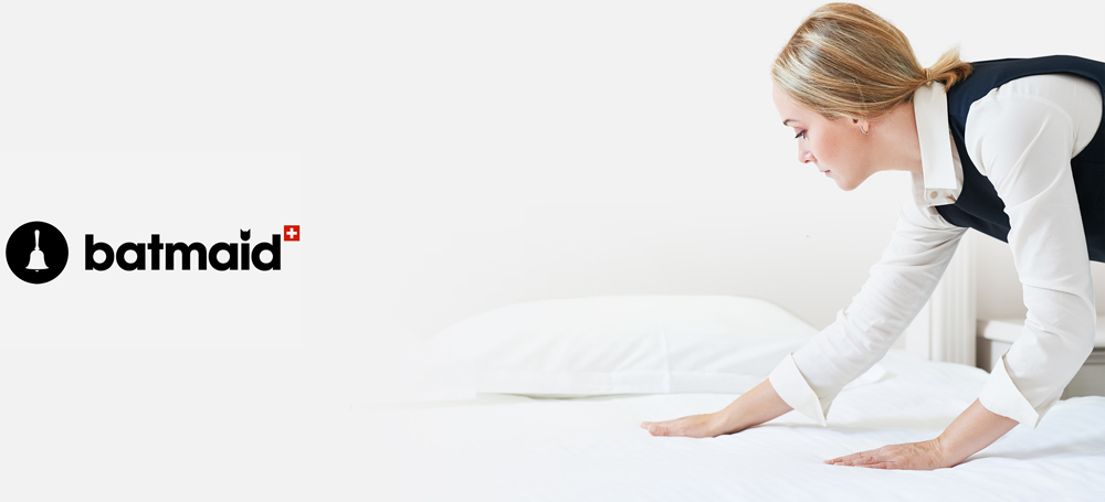 Housekeeper in uniform prepares a luxury bed with white linens for GuestLee&rsquo;s premium Swiss rental in Verbier or Montreux. | GuestLee luxury rental Switzerland